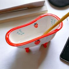 a red and white bowl with strawberries on it next to a cell phone, pencil holder and other items