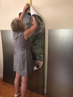 a woman in grey dress standing next to a wall with a surfboard on it