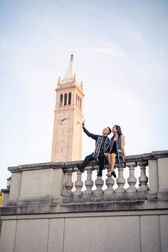 two people are sitting on a ledge near a clock tower