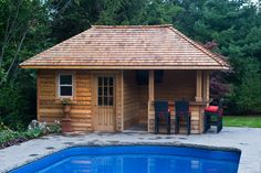 a small wooden cabin next to a swimming pool with chairs and tables around it,