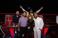 four people standing in front of a stage with their arms up and one person holding his hands out