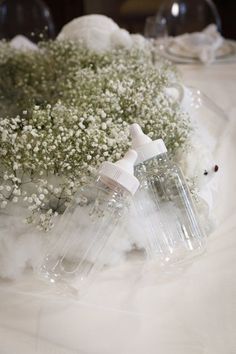 two baby's breath bottles sitting on top of a table covered in white flowers