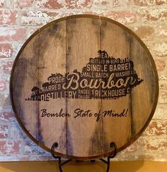 a wooden barrel sitting on top of a metal stand next to a brick wall with the words bourbon state of mind