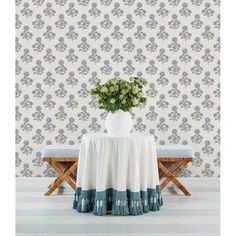 a white vase with green flowers sitting on top of a table next to a bench