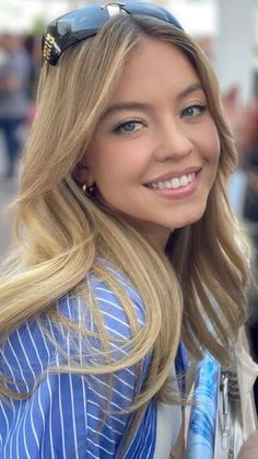 a woman with long blonde hair and sunglasses smiling at the camera while holding a cell phone