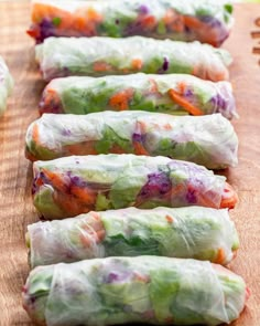 four rolls filled with vegetables sitting on top of a wooden cutting board