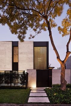 a modern house with black and white accents is lit up at night in front of a tree