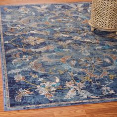 a blue rug with flowers on it in the middle of a wooden floor next to a vase