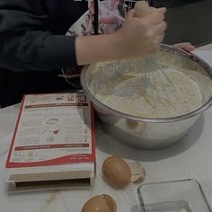 a person mixing batter in a bowl on top of a table next to an egg carton