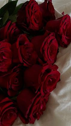 a bunch of red roses laying on top of a white sheet