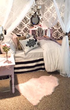 a white bed sitting under a canopy next to a table with a vase on it