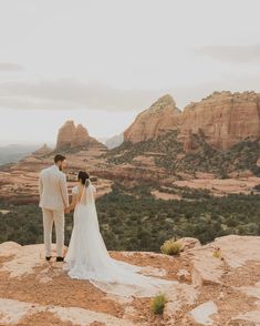 a bride and groom standing on top of a mountain