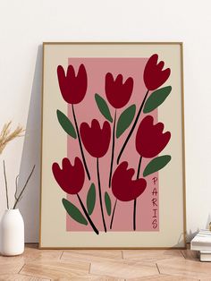 a painting with red flowers on a pink background next to a white vase and some books