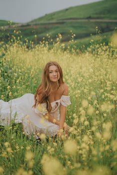 a beautiful young woman sitting in the middle of a field full of yellow wildflowers