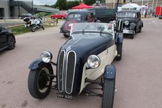 an antique car is parked in a parking lot with other cars behind it and people standing around