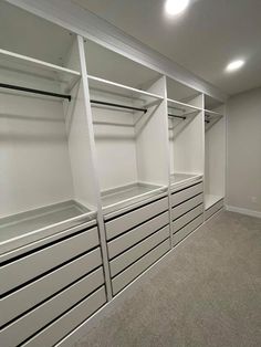 an empty walk in closet with white shelves and drawers