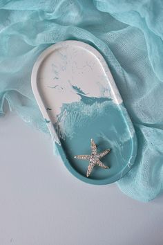 a starfish brooch sitting on top of a blue cloth next to a white plate