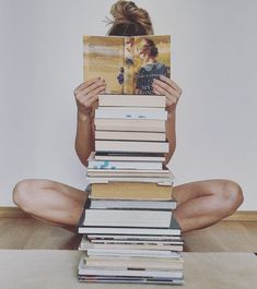 a woman sitting on the floor reading a book with stacks of books in front of her