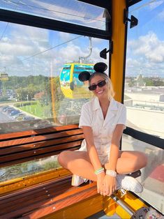 a woman sitting on top of a wooden bench in front of a cable car window