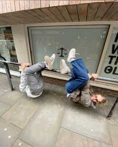 two young boys playing on the sidewalk in front of a store with their feet up