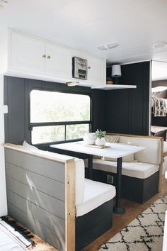 the interior of a travel trailer with white furniture and black walls, including a dining table