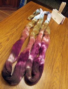 four pieces of dyed wool sitting on top of a wooden table next to an electronic device