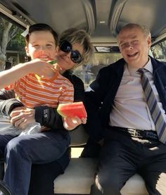 three people sitting on a bus eating watermelon and drinking ice cream from a straw