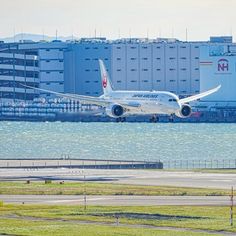 an airplane is taking off from the runway in front of a large building and body of water