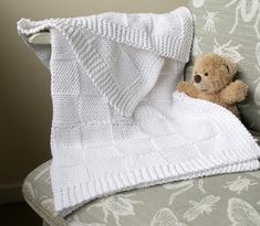 a teddy bear is sitting under a blanket on a couch with a white knitted blanket