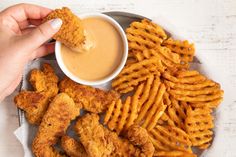 a person dipping sauce on some fried chicken nuggies and french fries with dip