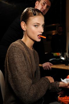 a woman sitting at a desk with carrots in her mouth