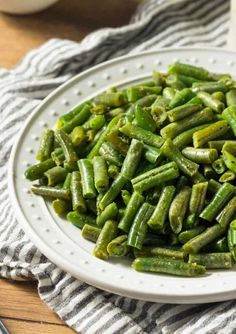 a white plate topped with green beans on top of a wooden table next to a glass of milk