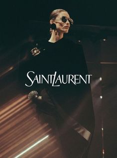 a man in black shirt and sunglasses standing next to a wall with the word saint laurent on it