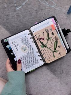 a person is holding an open notebook with drawings on it and writing in the pages