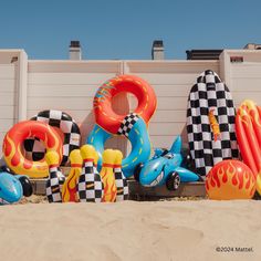 an assortment of inflatable letters on the sand near a building with a checkered wall