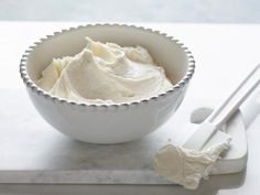 a white bowl filled with whipped cream next to two spoons on top of a counter