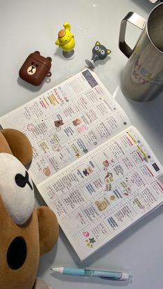 a teddy bear sitting on top of a desk next to an open planner and pen