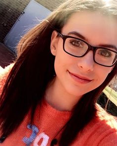 a woman with glasses is smiling for the camera while wearing an orange sweater and black rimmed glasses