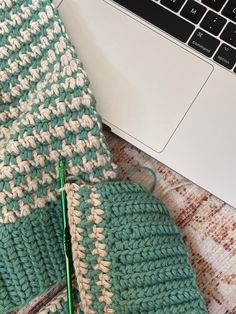 an open laptop computer sitting on top of a table next to a crocheted blanket