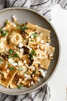 a bowl filled with pasta covered in feta cheese and parsley on top of a striped towel