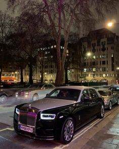 a row of cars parked on the side of a city street at night with buildings in the background