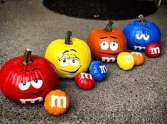 four pumpkins with faces painted to look like m and m are lined up on the ground