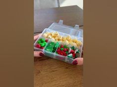 a person holding a plastic container filled with assorted candies on top of a wooden table