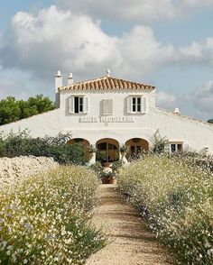 a white building with lots of plants and flowers around it's front entrance on a sunny day