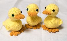 three crocheted yellow ducks sitting next to each other on a white cloth background