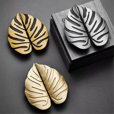 three gold and silver leaf magnets sitting on top of a wooden box next to each other