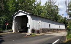 a white covered bridge crossing over a road in the middle of trees and bushes on both sides