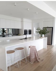 a white kitchen with two stools next to the counter top and an island in front of it