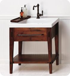 a bathroom sink sitting under a faucet on top of a wooden table next to a white wall