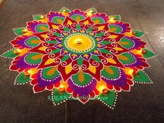 a brightly colored flower design on the ground with candles lit up in front of it